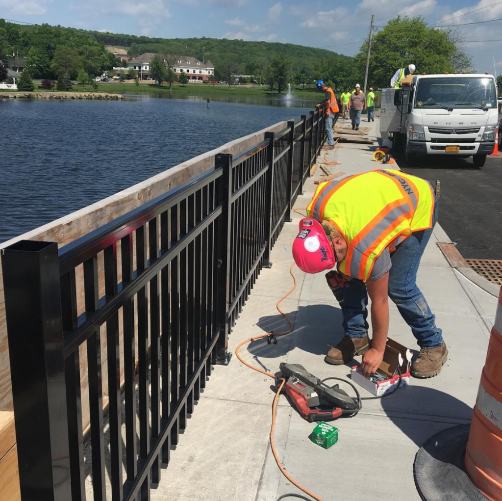 workers installing black aluminum fence along sidewalk
